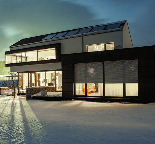 Abendlich beläuchtetes Haus im Winter mit halb heruntergelassenen Rollläden