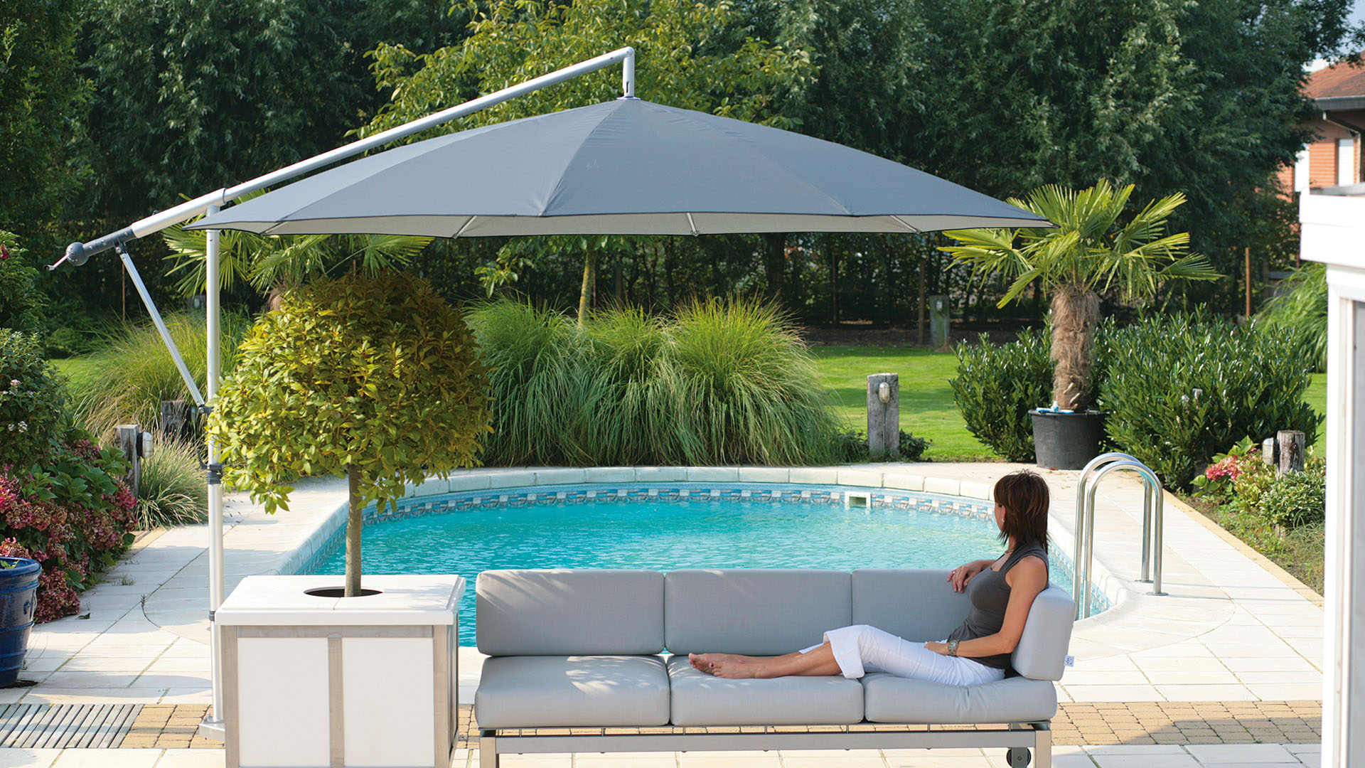 Eine Frau blickt von ihrem schirmgeschützten Terrassensofa aus zu einem Swimming Pool